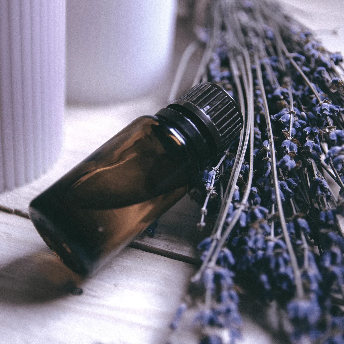 An amber bottle of essential oil resting on pale wood beside dried lavender